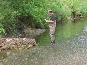 This image shows a person documenting findings while inspecting an outfall