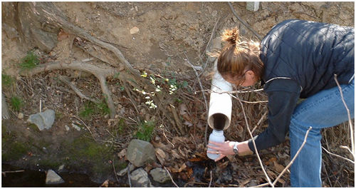 This image shows a person collecting a water sample from an outfall